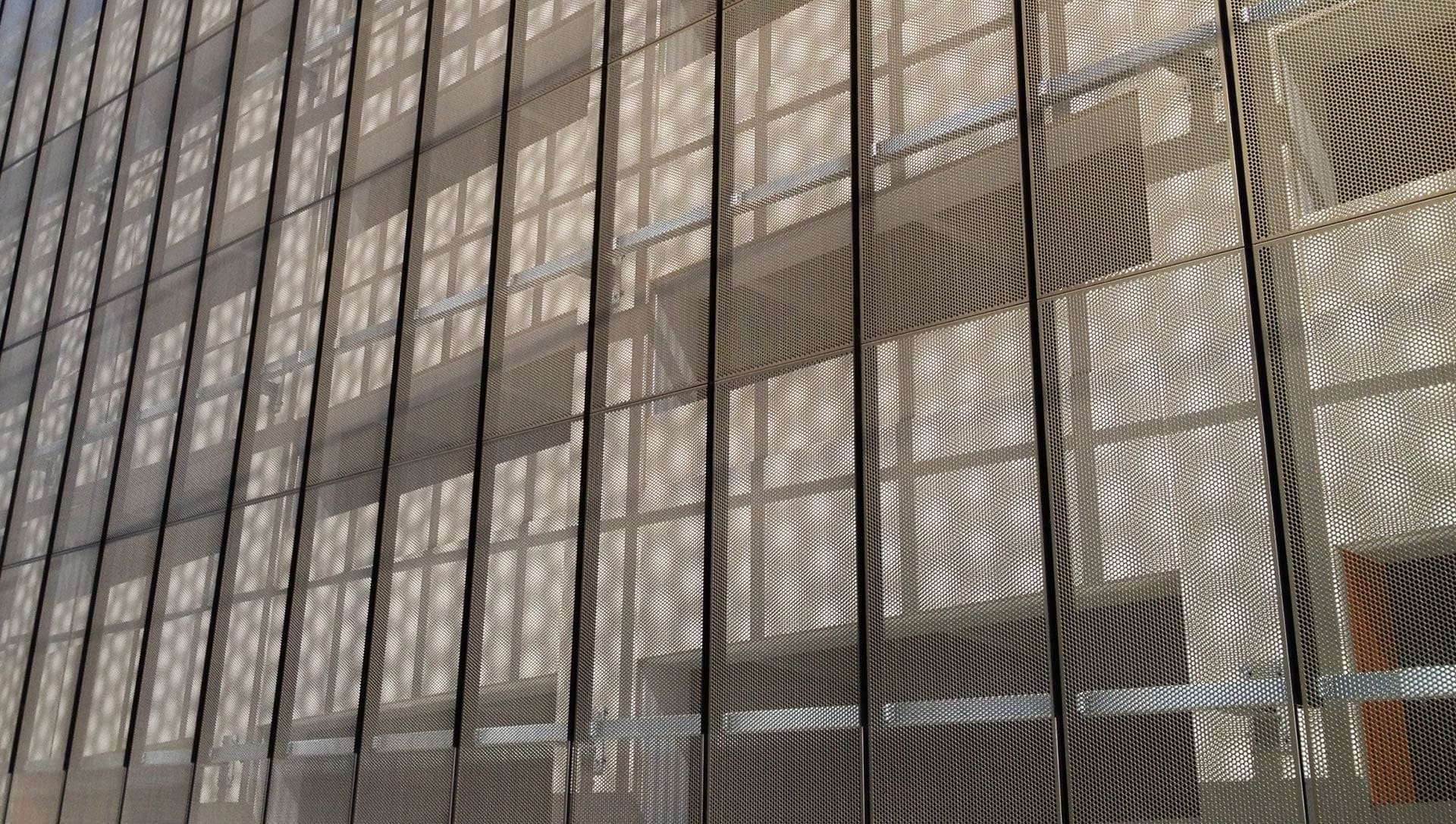 The perforated metal panel's shadow creates a moire effect against the building's surface.
