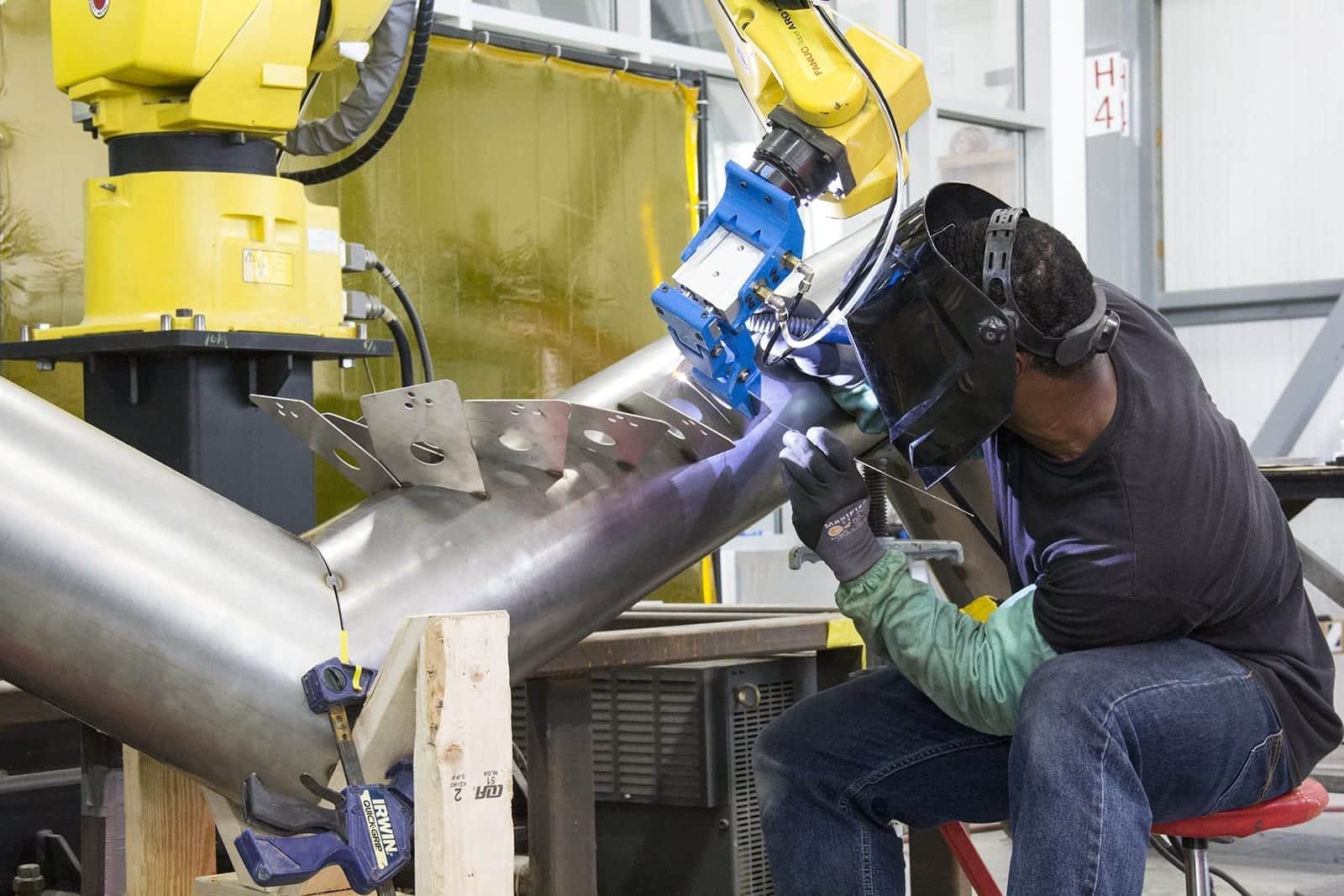 Local 2 Journeyman Keidric Rowe welds stainless steel tab while Fanuc robot holds in position