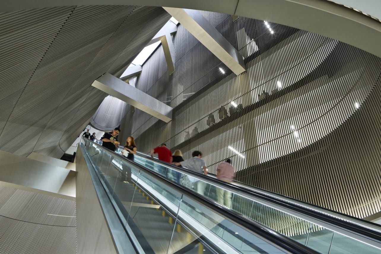 Daylight illuminates the escalator space, amplifying the glow of the gold anodized aluminum.